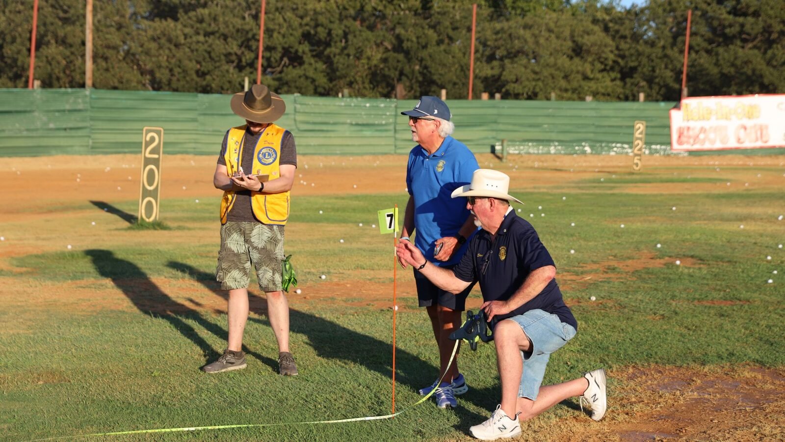 Lions volunteers in Lions vests and shirts measure a shot from the pin with a tape at the 2026 Hole-in-One Shootout