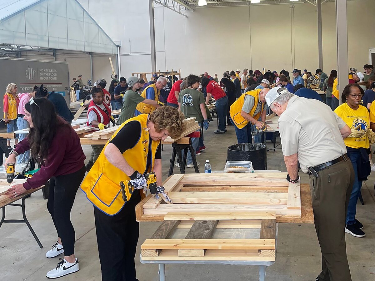 Colleyville Lions in gold vests drilling and assembling wooden bed frames alongside other volunteers at a Sleep in Heavenly Peace bed build