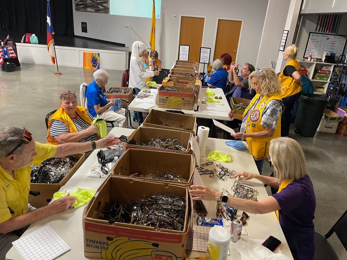 Colleyville Lions in gold vests sorting and cleaning donated eyeglasses from boxes along long tables